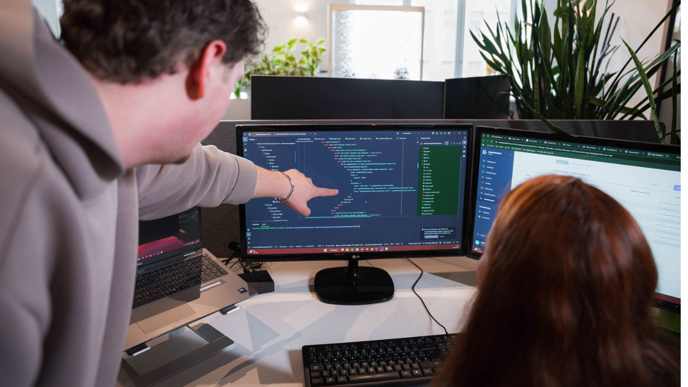 Experimente in Shopware 6 Ein Kollege hilft einer Mitarbeiterin beim programmieren.